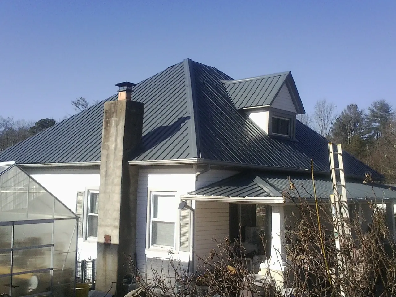 Dark blue standing seam metal roof on a white farmhouse with dormer — Slate & Tile Roof Repair by Roofing Brothers in North Palm Springs