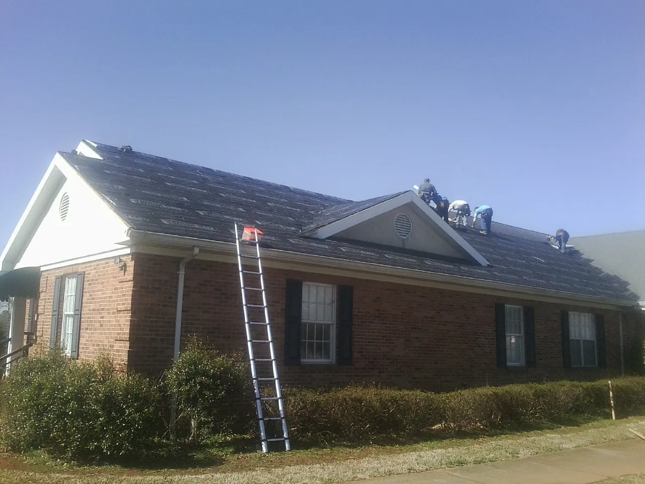 Crew tearing shingles off a brick ranch roof with a ladder set — Emergency Roof Repair work by our crew in North Palm Springs