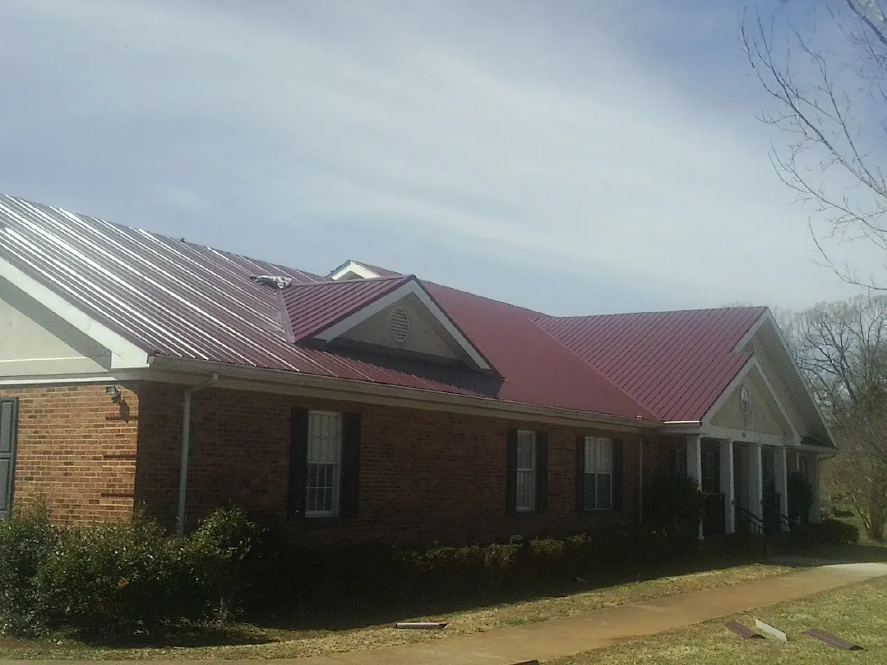 Red metal roof with gabled entries on a long brick building, from a Hail Damage Roof Repair job in North Palm Springs