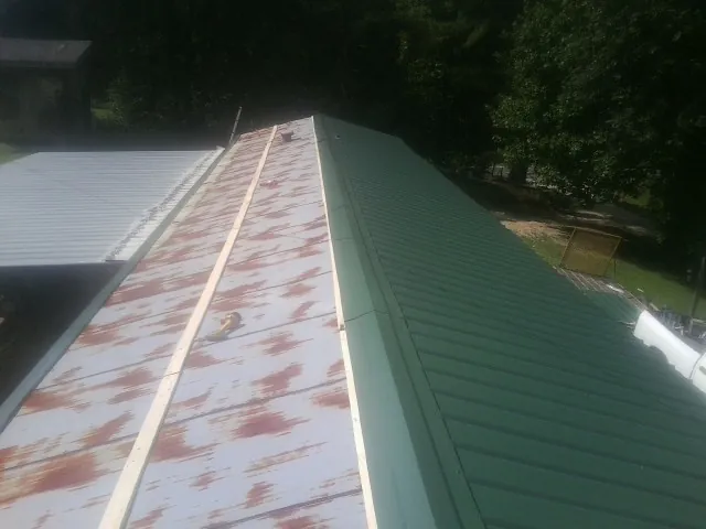 Old rusted panels beside newly installed green metal roofing — Wind Damage Roof Repair by Roofing Brothers in North Palm Springs
