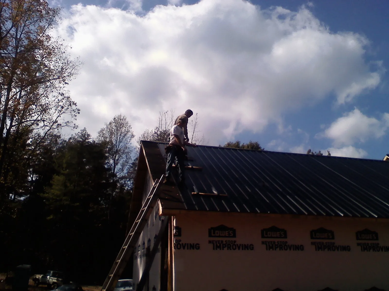 Roofer fastening dark metal panels high against a cloudy sky, from a Roof Inspection job in North Palm Springs